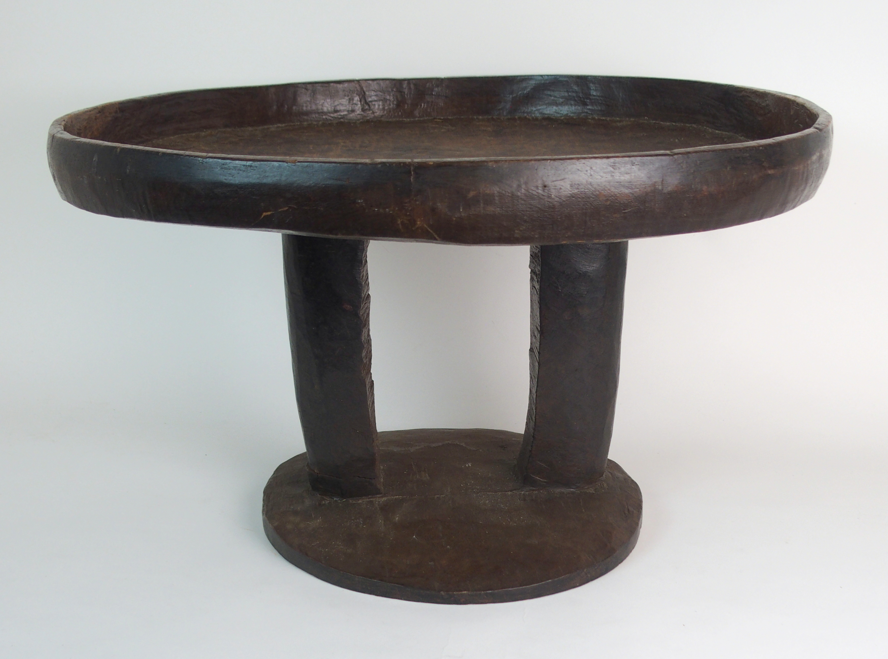 *WITHDRAWN* AN AFRICAN TRIBAL HARDWOOD CIRCULAR TABLE with deep carved rim above a pair of curved