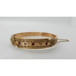 A 9ct gold Etruscan design bangle set with rose cut diamonds and red gems, inner dimensions 5.8cm