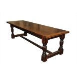 A large reproduction refectory oak dining table, the thick planked top overhanging a shallow