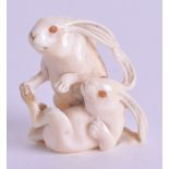 A 19TH CENTURY JAPANESE MEIJI PERIOD CARVED IVORY NETSUKE modelled as two hares with amber eyes. 3.5