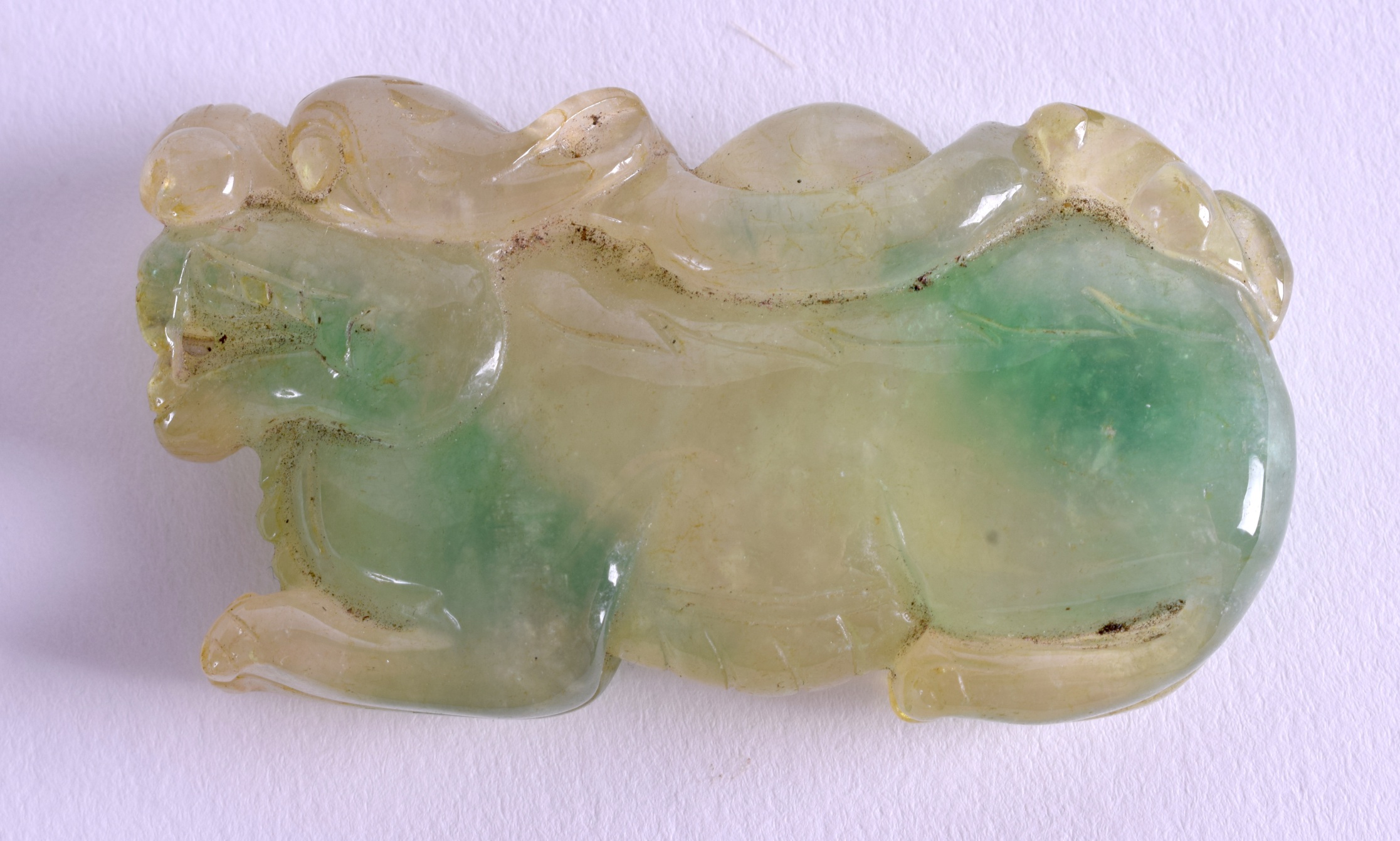 A CHINESE CARVED JADEITE BEAST AMULET. 6 cm wide.