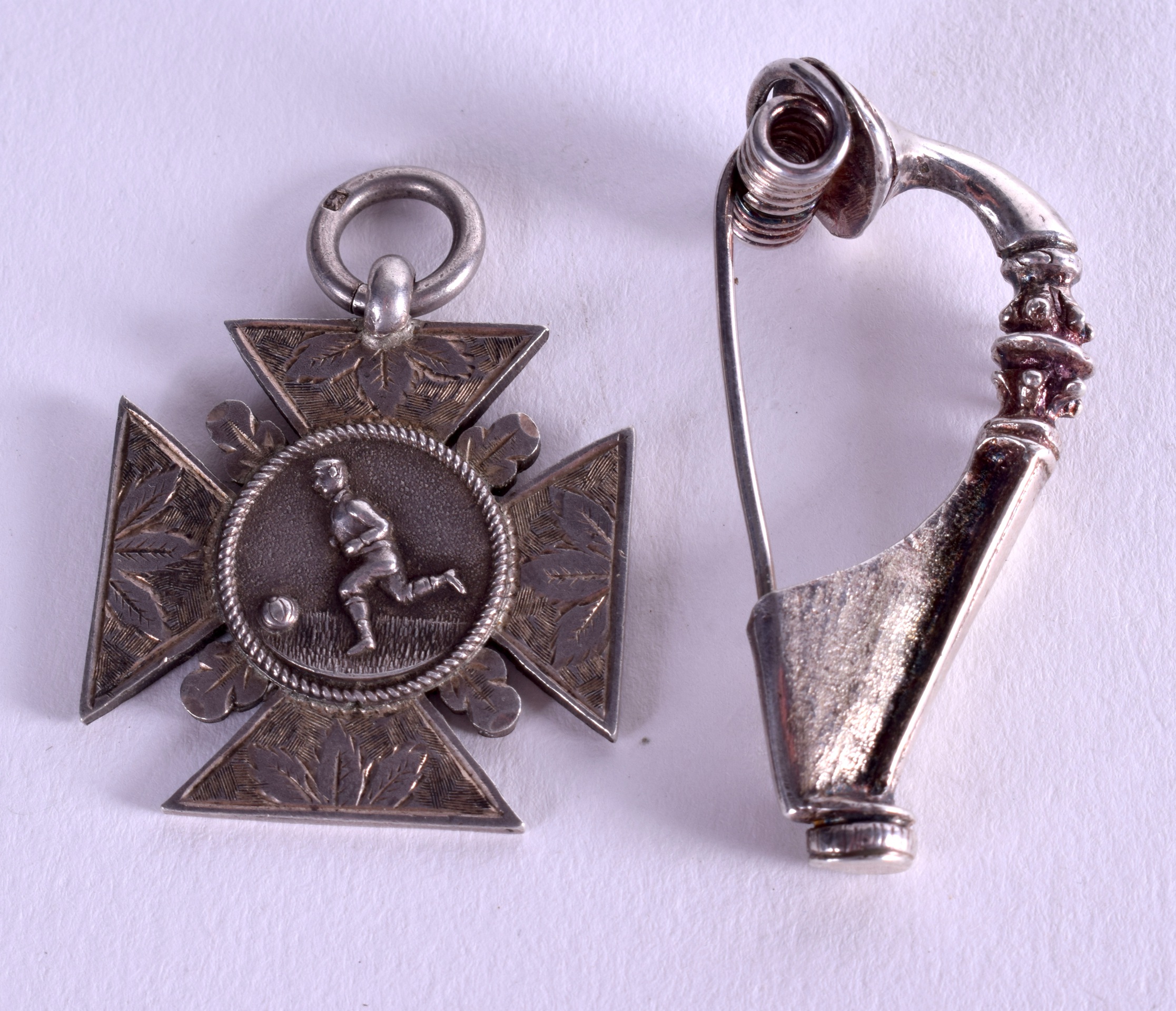 AN ANTIQUE SILVER FOOTBALLMEDAL together with a silver brooch. (2)