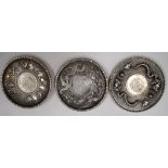 THREE CHINESE WHITE METAL DISH, each inset with a coin. 10 cm wide. (3)