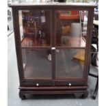 AN EARLY 20TH CENTURY CHINESE HARDWOOD DISPLAY CABINET ON STAND, formed with porcelain handles. 125