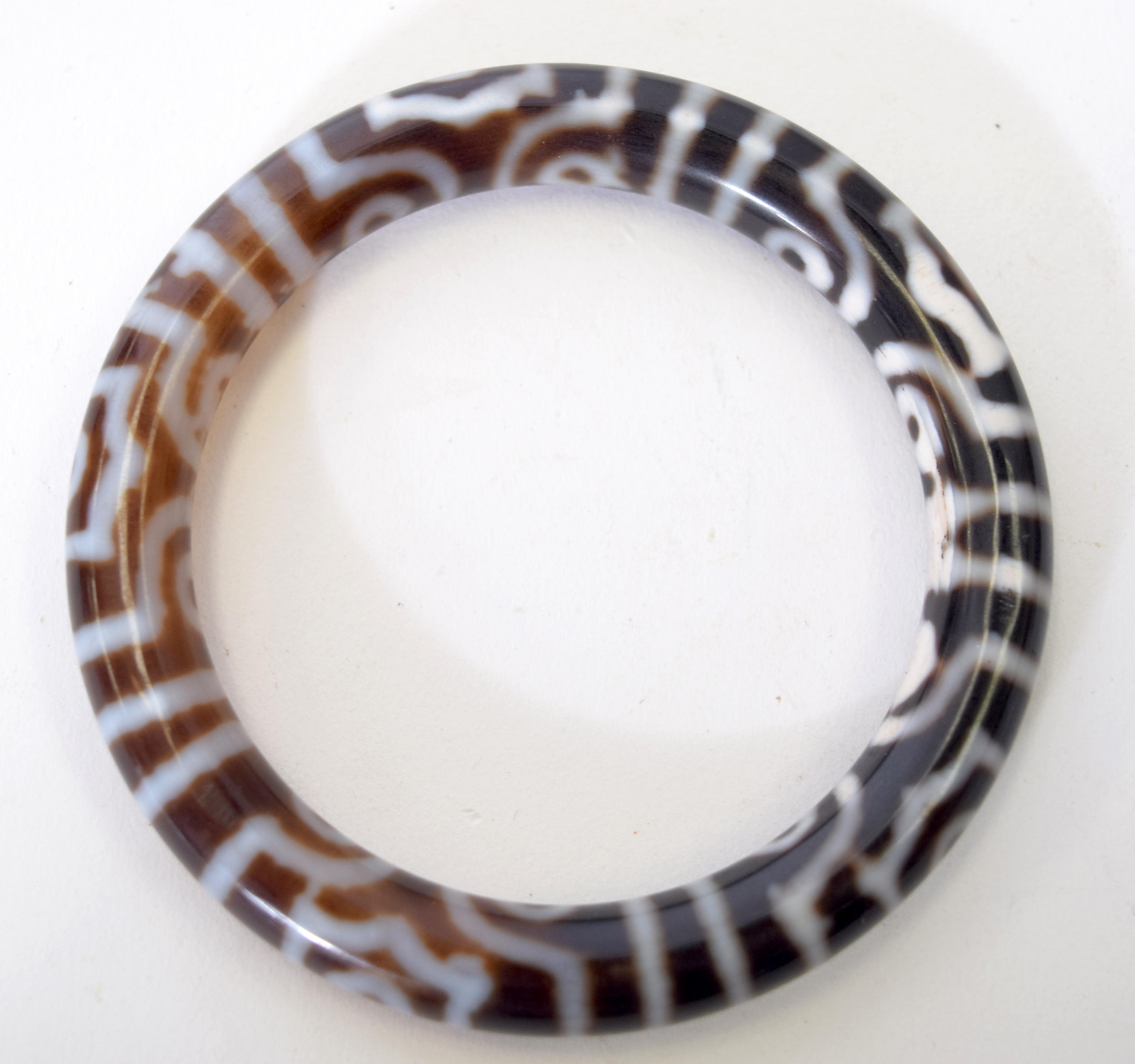 AN EARLY 20TH CENTURY TIBETAN AGATE BANGLE, decorated with symbols. 8.5 cm wide.