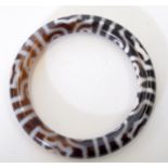 AN EARLY 20TH CENTURY TIBETAN AGATE BANGLE, decorated with symbols. 8.5 cm wide.