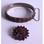 AN ANTIQUE SILVER AND GARNET BANGLE with a matching brooch. 6.5 cm & 3.5 cm wide. (2)