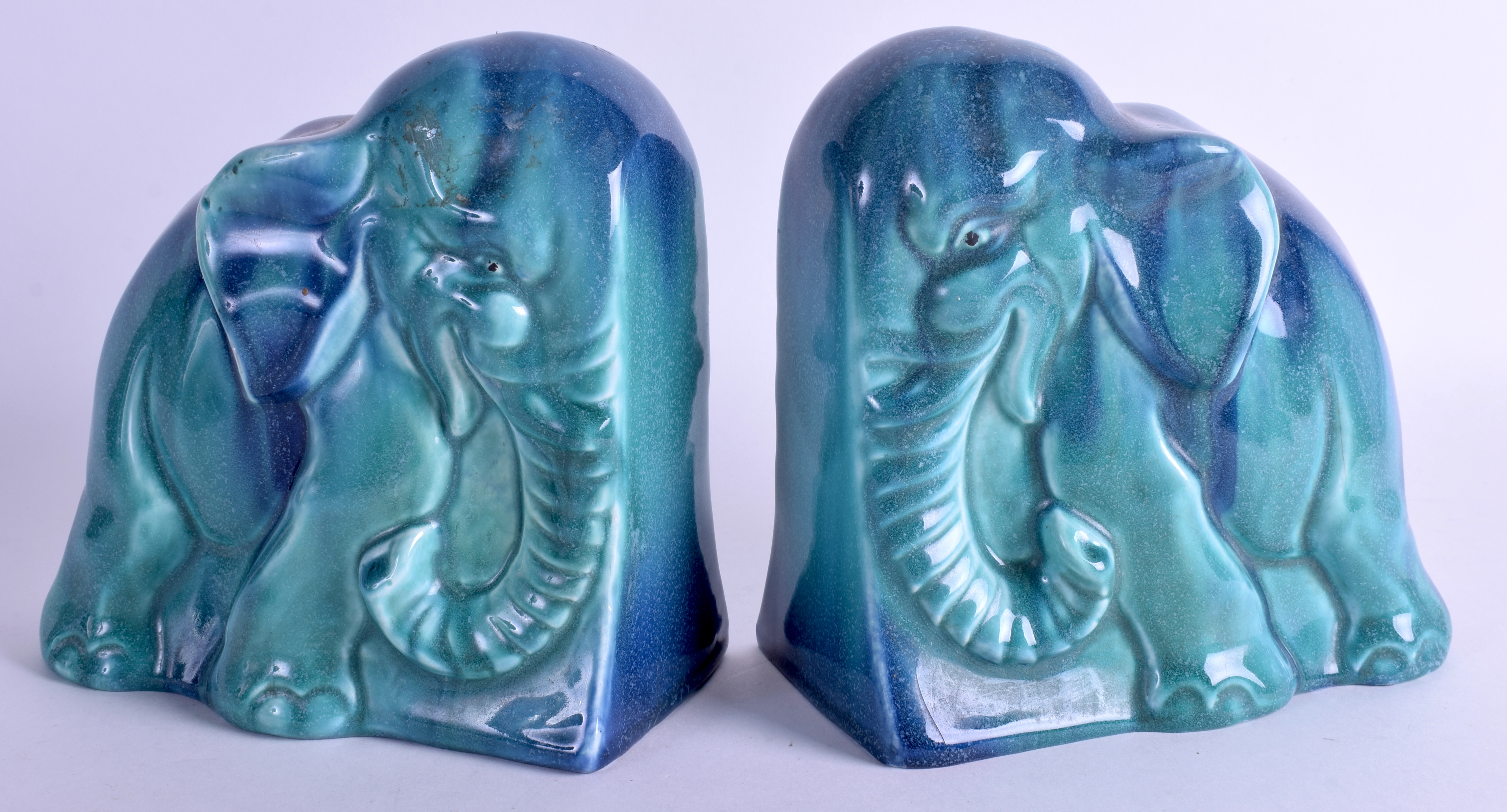 AN UNUSUAL PAIR OF 1950S CONTINENTAL BLUE GLAZED FLAMBE POTTERY BOOKENDS in the form of elephants.