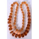 AN EARLY 20TH CENTURY CARVED AMBER NECKLACE, formed with facetted beads. 72 cm long and weight 77 g