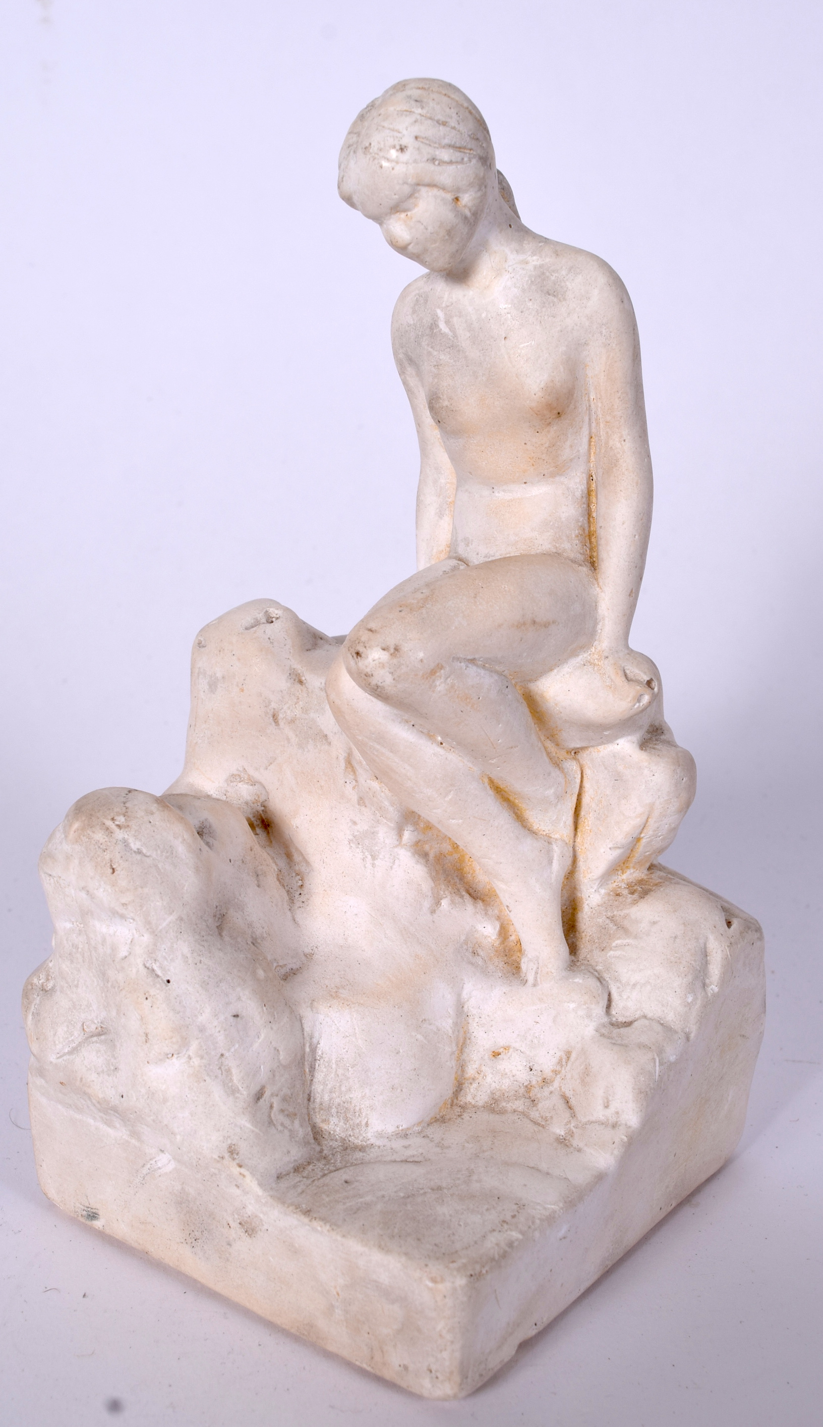 AN EARLY 20TH CENTURY PLASTER FIGURE OF A SEATED FEMALE, modelled upon rocks. 18 cm high.