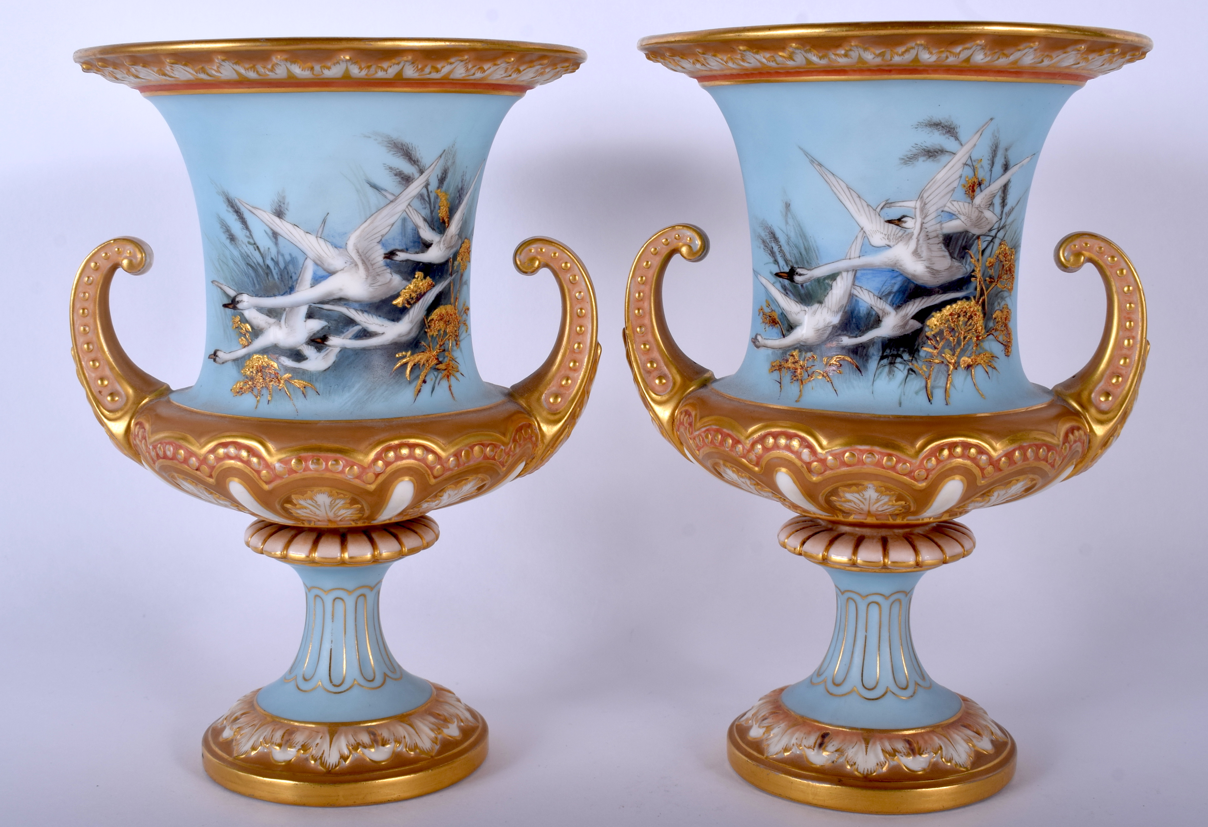 A PAIR OF ROYAL WORCESTER TWIN HANDLED PORCELAIN URN VASES by Charles Baldwyn, painted with swans.
