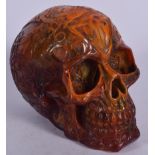AN AMBER TYPE SCULPTURE OF A SKULL, formed with gothic decoration. 13 cm x 16 cm.