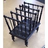 AN ARTS & CRAFTS EBONISED WOODEN CANTERBURY, formed with turned legs and brass casters. 52 cm wide.