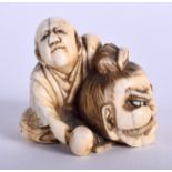 A 19TH CENTURY JAPANESE MEIJI PERIOD CARVED IVORY NETSUKE modelled as a male holding a samurai mask.