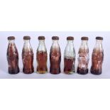 SEVEN MINIATURE COCA COLA BOTTLES. 6 cm wide.