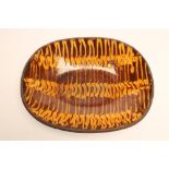 AN ENGLISH COUNTRY SLIPWARE DISH, of rounded oblong form, with three yellow slip trails on a brown