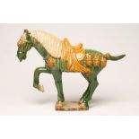 A TANG STYLE EARTHENWARE HORSE standing with right fore-leg raised and with saddle and bridle, in