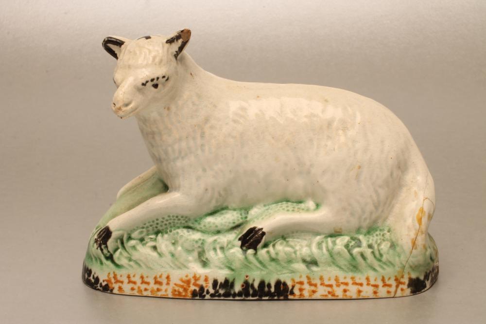 A YORKSHIRE PEARLWARE SHEEP, c.1790, recumbent on a naturalistically moulded base painted in Pratt