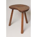 AN ADZED OAK STOOL by Wilf Hutchinson, the mildly dished kidney shaped seat raised on three