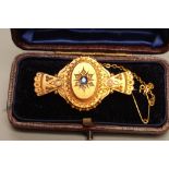 A VICTORIAN BROOCH, the central oval boss gypsy set with a cushion cut sapphire within a border of