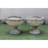 A PAIR OF COMPOSITION STONE URNS, the bowl moulded with foliage in relief beneath a cable twist rim,