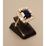 AN ART DECO SAPPHIRE AND DIAMOND CLUSTER RING, the square cut sapphire claw set to a border of