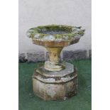 A VICTORIAN SANDSTONE URN of circular faceted form, the shallow bowl with broad fluted rim, on