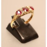 A THREE STONE RUBY RING, the facet cut stones with four diamond points between to scroll carved