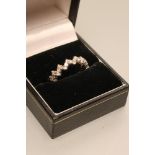 A DIAMOND ETERNITY RING, the zig-zag shank claw set with numerous small brilliant cut stones to an