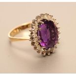 AN AMETHYST AND DIAMOND CLUSTER RING, the oval facet cut amethyst claw set to a border of twenty two