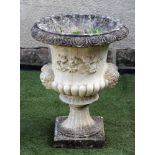 A COMPOSITION STONE URN of half fluted campana form with mask handles and square base, 19" x 25 1/2"