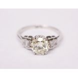 A PLATINUM DIAMOND RING with central round cut diamond complimented by baguette cut shoulders, 1.