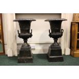 A PAIR OF GARDEN URNS, raised on short plinths, black colour, 34" tall, 17" diam approx