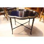 A GILT & BACK METAL TRAY ON A BAMBOO STYLE TABLE, with raised gallery rim, scallop shaped, 30" x 25"
