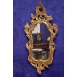 A GILTWOOD WALL MIRROR, with pierced and carved frame, having foliage & scroll details, 35" x 16.