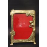 AN ART NOUVEAU STYLE BRASS PICTURE FRAME, with figure of a lady and floral design, 10" x 7.5" approx