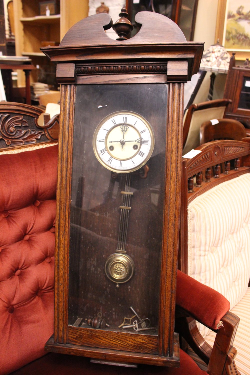 A BOXED WALL CLOCK, with turned finial to the top, brass and enamel face, keys within, 36" x 14" x