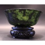 A SPINACH JADE BOWL, sitting on a carved wooden stand, 5" diameter approx