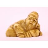 A NETSUKE OF A MAN, with beard, seated cross legged with his arm resting on a parcel, 1.25" long, 1"