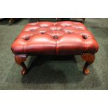 A BUTTON TOPPED RED LEATHER 'CHESTERFIELD' FOOT STOOL, with short cabriole shaped legs and brass