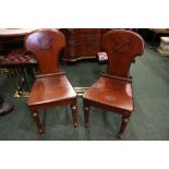 A PAIR OF HALL CHAIRS, with carved crest motif to the backs, raised on turned front legs, sabre