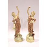 A PAIR OF ROYAL BOHEIMIAN FIGURINES, each depicts a lady holding flowers aloft, standing on a