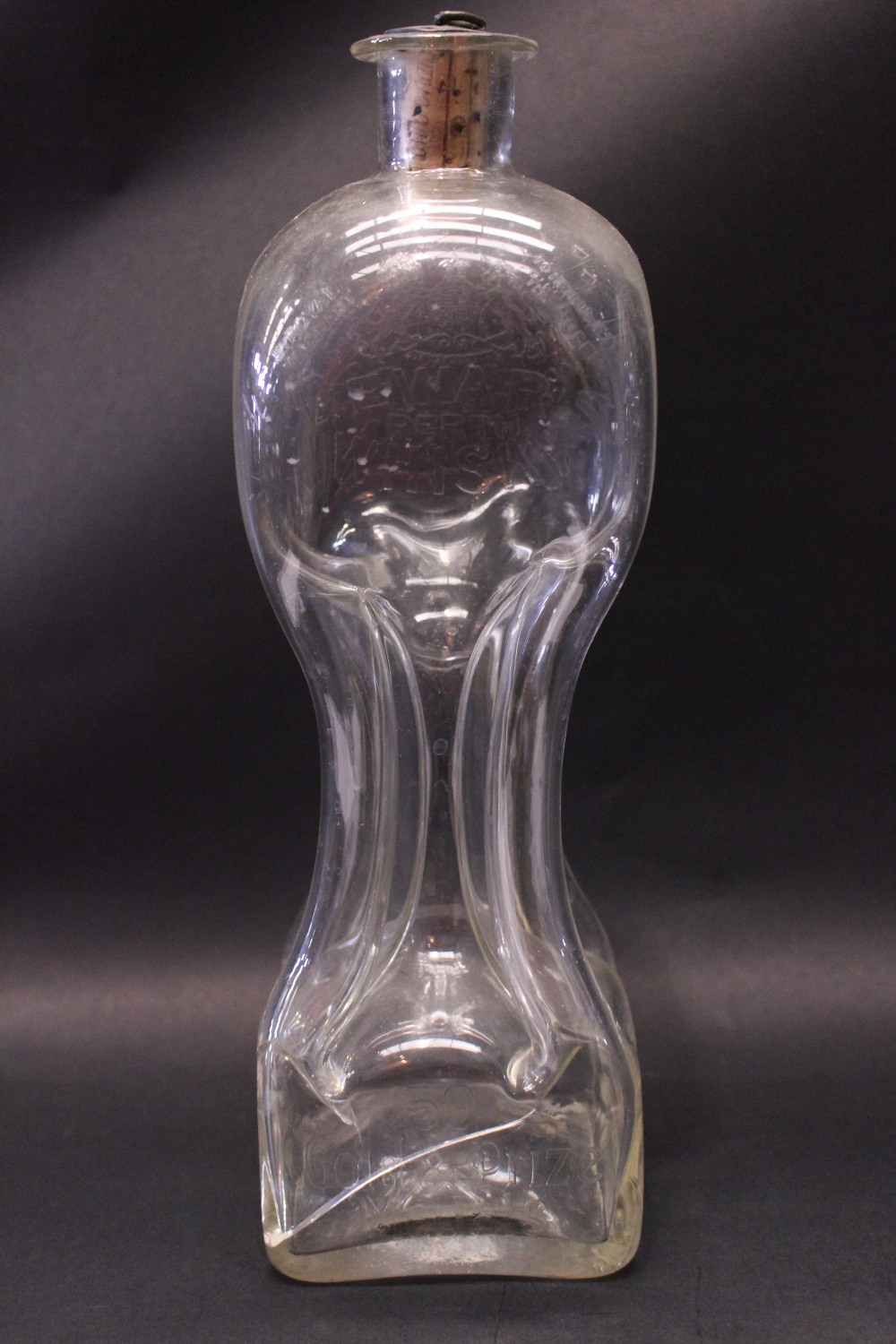 A ‘DEWARS WHISKY’ PINCHED ‘HOUR GLASS’ DECANTER, with corked stopper, having an Italian coin on