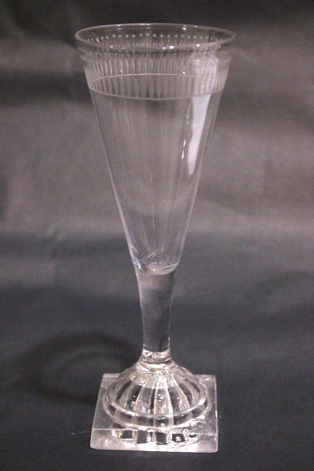 A TAPERED GLASS FLUTE, with cut detail to the rim, raised on a lemon squeeze foot / base, 7" tall