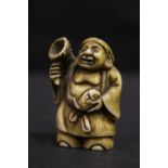 A NETSUKE OF A FISHERMAN holding a net and fish, 2" tall approx
