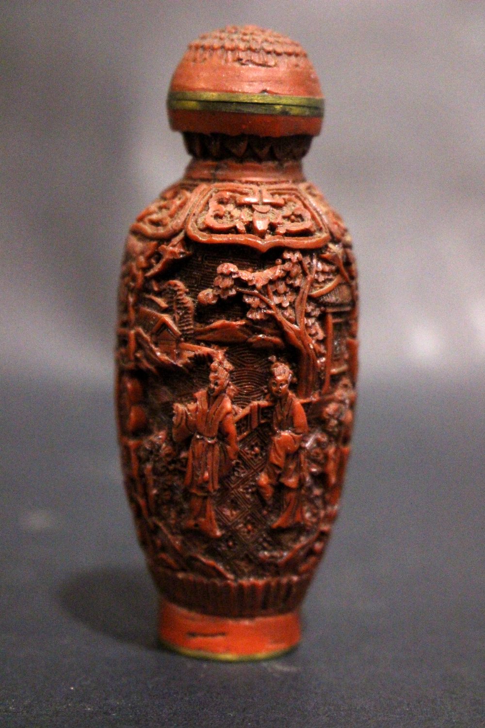 A CARVED CINNABAR & BRASS SNUFF BOTTLE, with inlaid brass character marks to the base, decorated