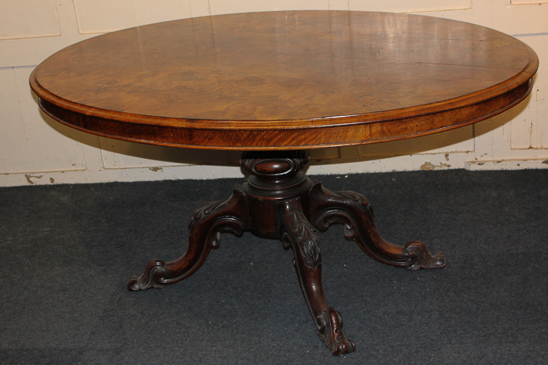 A Victorian walnut dining table with oval tilt-top on baluster stem and four carved outswept legs to