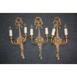 A set of four 19th century style gilt metal two-branch wall lights with ribbon, tassel and scrolling