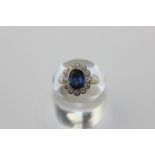 A sapphire and diamond cluster ring, the oval cut stone rubover set within a border of brilliant