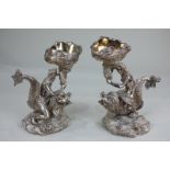 A pair of silver plated figures of a semi-nude man and woman riding dolphins and holding conch